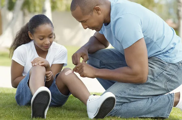 Padre attaccare fasciatura a figlia ginocchio a parco — Foto Stock