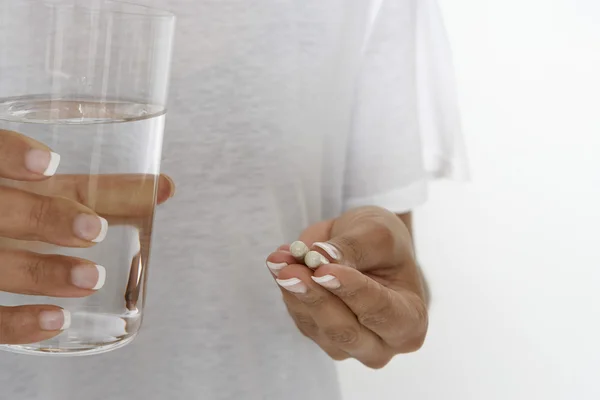 Mujer sosteniendo píldoras y vaso de agua —  Fotos de Stock