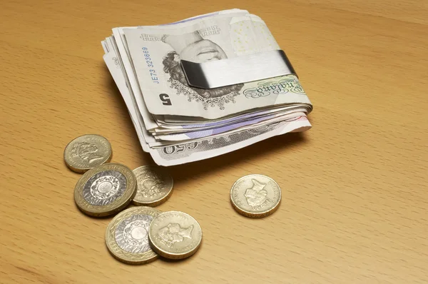 Валюта в денежном клипе и монеты на столе — стоковое фото