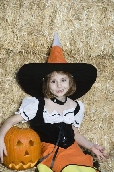 Flicka i halloween outfit sitter av hö med jack-o-lantern — Stockfoto