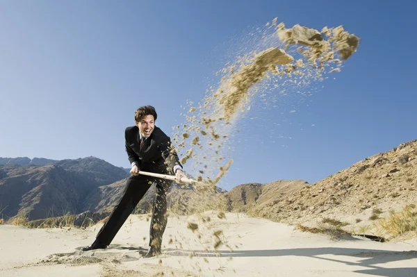 Zakenman met behulp van een schop in de woestijn — Stockfoto