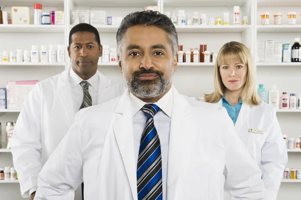 Три уверенных фармацевта, стоящих в аптеке — стоковое фото