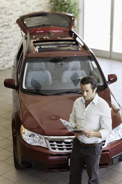 Hombre adulto medio que lee el documento delante del coche de lujo en la sala de exposición —  Fotos de Stock