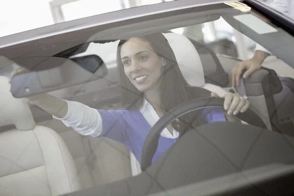 Vrouw rearview spiegel van haar nieuwe auto aanpassen — Stockfoto