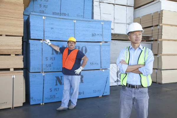 Manliga lagerarbetare står framför stack av plywood — Stockfoto