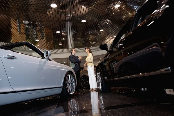 Salesman talking to woman in automobile showroom — Stock Photo, Image