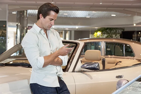 Чоловік стоїть поряд з машиною зі своїм мобільним телефоном — стокове фото