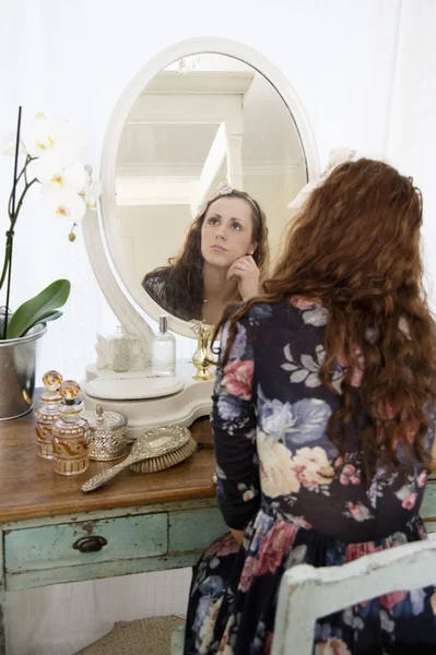 Задумчивая молодая женщина сидит перед зеркалом — стоковое фото