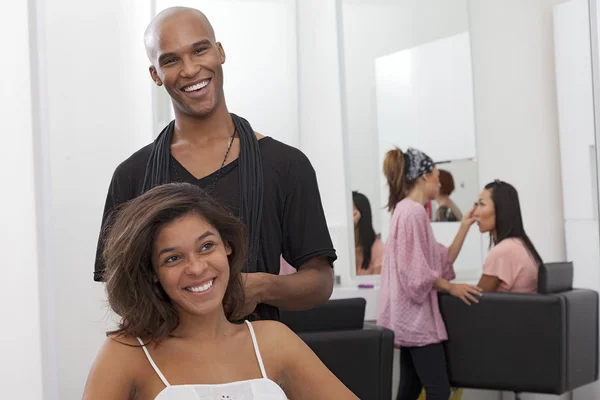 Jeune femme assise sur une chaise avec coiffeur debout derrière — Photo