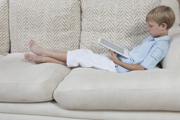 Мальчик с цифровым планшетом на диване — стоковое фото