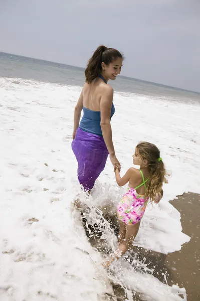 Mãe e filha caminhando através do surf — Fotografia de Stock