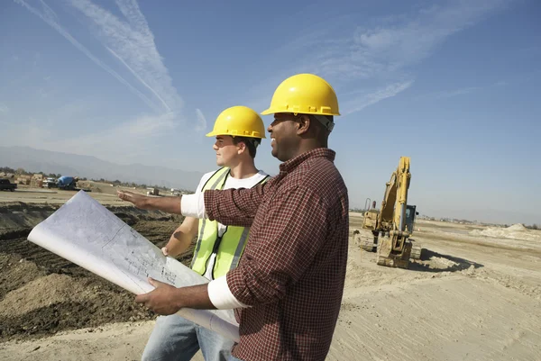 Trabajadores con sombreros duros mirando el plan en el sitio — Foto de Stock