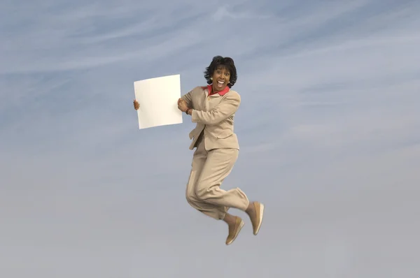 Businesswoman jumping with blank sign — Stock Photo, Image