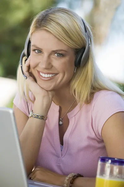 Kulaklıklı mikrofon seti ile dizüstü bilgisayar kullanan kadın — Stok fotoğraf