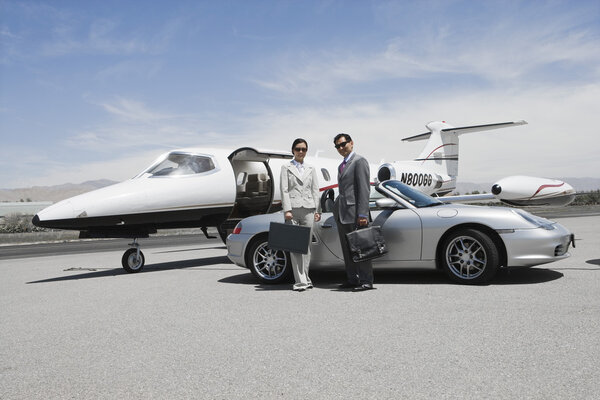 Business couple in front of convertible and private jet