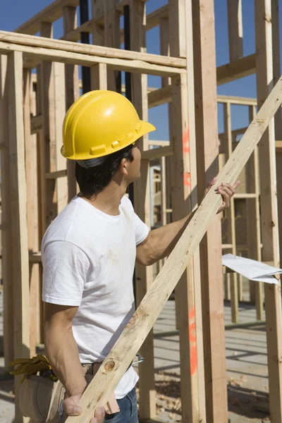 Arbeiter hält Planke auf Baustelle hoch — Stockfoto