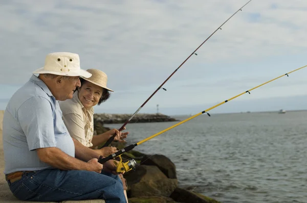 Vista lateral de la feliz pareja de ancianos pesca contra el cielo nublado — Foto de Stock