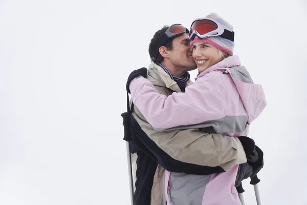 Side view of a happy couple in warm clothing embracing in snow — Stock Photo, Image