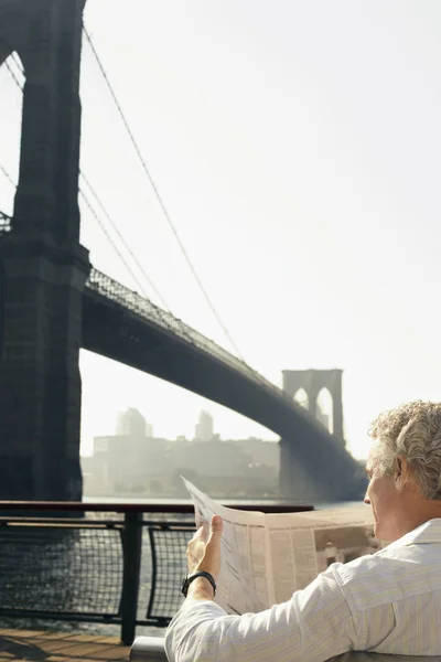 Man reading newspaper by Brooklyn Bridge — Stock Photo, Image