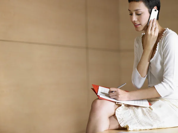 Mujer de negocios en el teléfono celular tomando notas — Foto de Stock