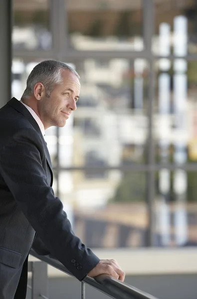 Businessman leaning on railing in office — Stock Photo, Image