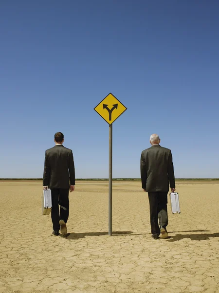 Businessmen with briefcases walking past road sign — Stock Photo, Image
