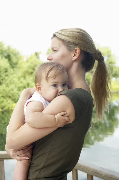 Mãe segurando filha por lago — Fotografia de Stock