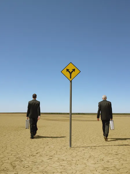 Businessmen with briefcases walking past road sign — Stock Photo, Image
