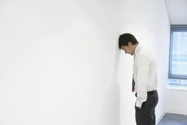 Unhappy Businessman with head against wall