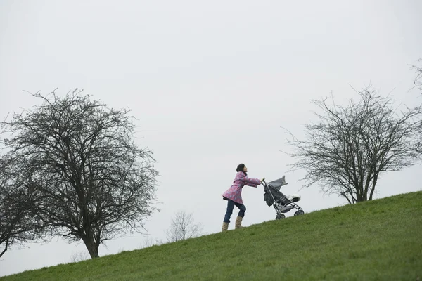 Mother pushing stroller uphill — Stock Photo, Image