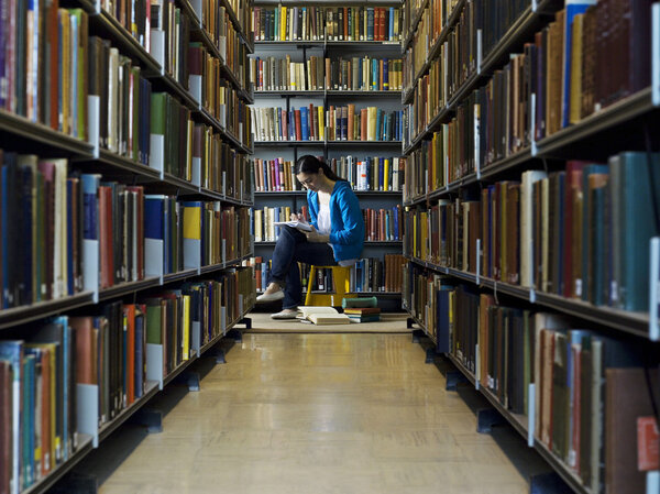 Woman reading by bookshelf Stock Image