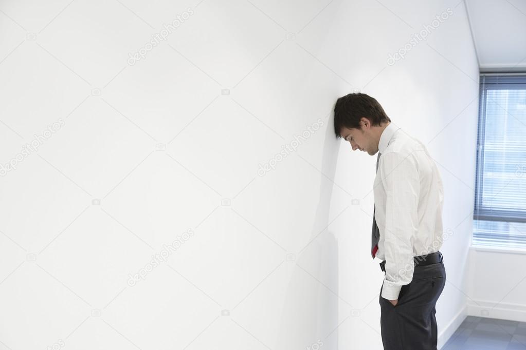 Unhappy Businessman with head against wall