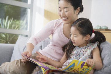 Mother sitting with daughter reading a book clipart