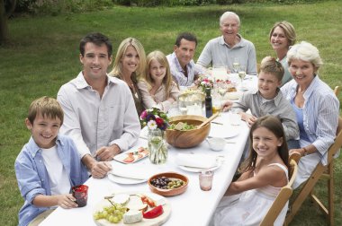 Three generation family dining in garden clipart