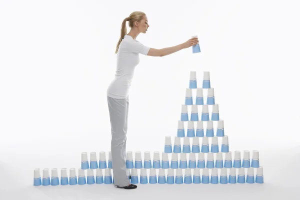 Vrouw stapelen plastic bekers piramide — Stockfoto