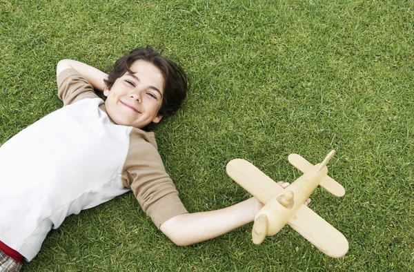 Pojken ligga i gräset med leksak flygplan — Stockfoto