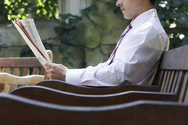 Businessman on bench reading newspaper — Stock Photo, Image