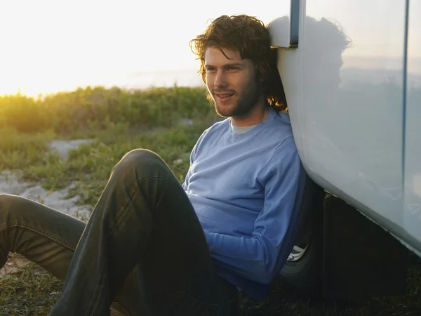 Man sitting on grass by wheel of van — Stock Photo, Image