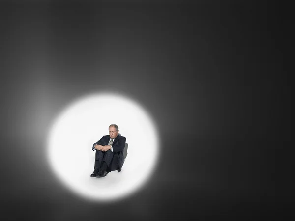 Businessman sitting in spotlight — Stock Photo, Image