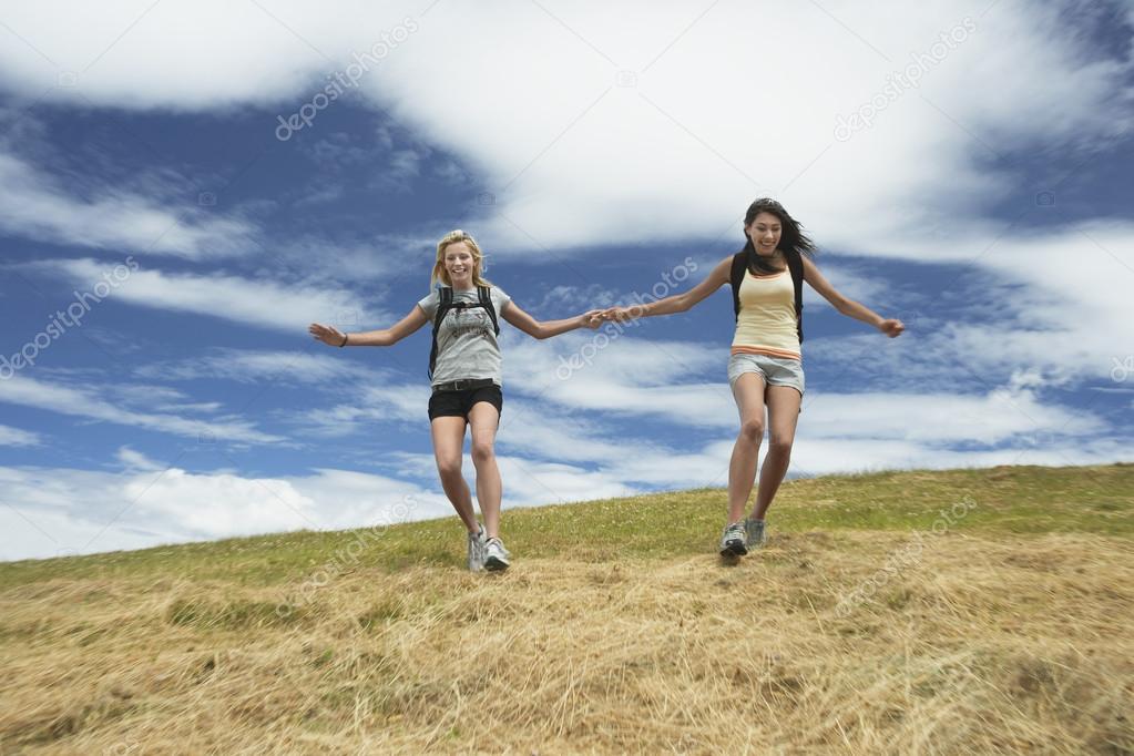 Two women holding hands skipping down hill