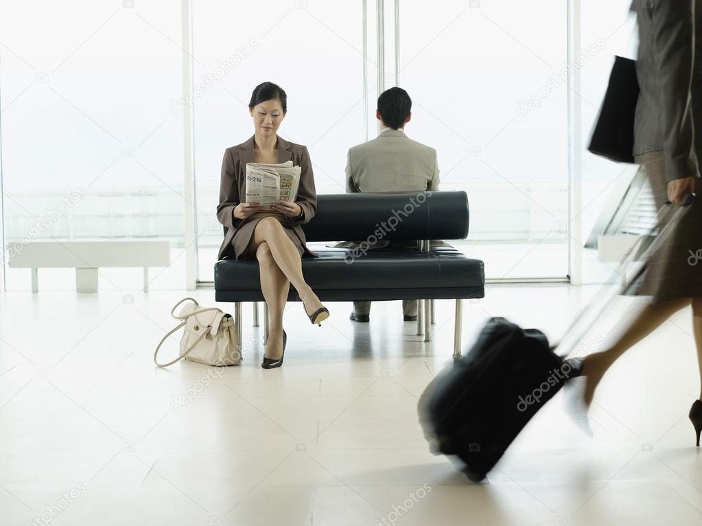 Businesswoman in airport reading newspaper