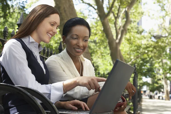 Женщины-коллеги используют ноутбук в парке — стоковое фото