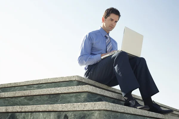 Mann sitzt mit Laptop auf Marmorplattform — Stockfoto