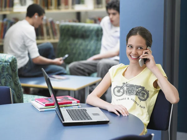 Girl using cell phone in library — Stock Photo, Image