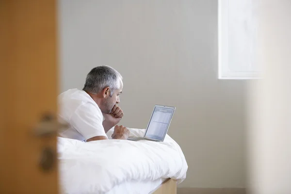 Mann benutzt Laptop auf Bett — Stockfoto