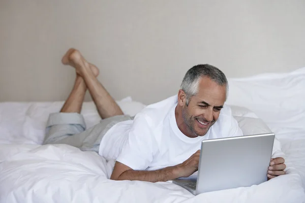 Mężczyzna korzystający z laptopa w łóżku — Zdjęcie stockowe