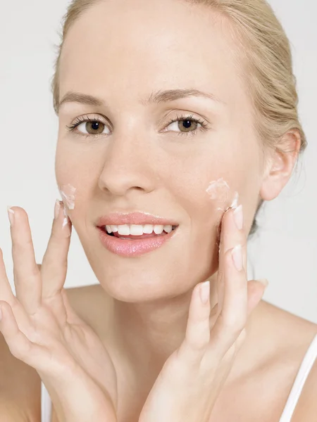 Mulher jovem aplicando creme facial — Fotografia de Stock