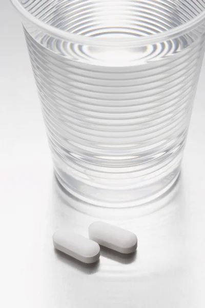 Pills beside water in plastic cup — Stock Photo, Image