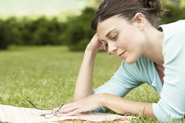 Frau liegt auf Gras und liest Zeitung — Stockfoto