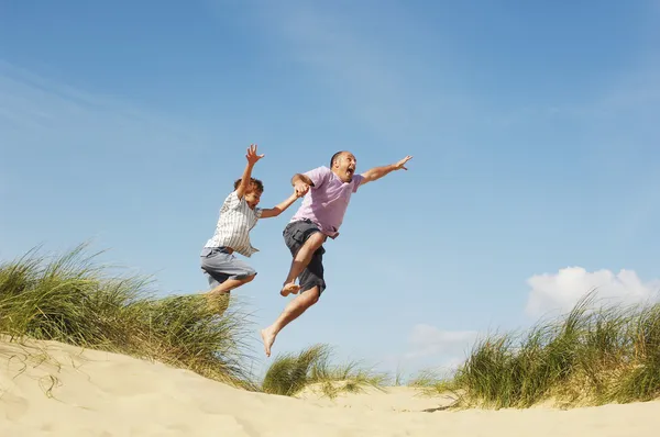 Vader en zoon springen op strand — Stockfoto